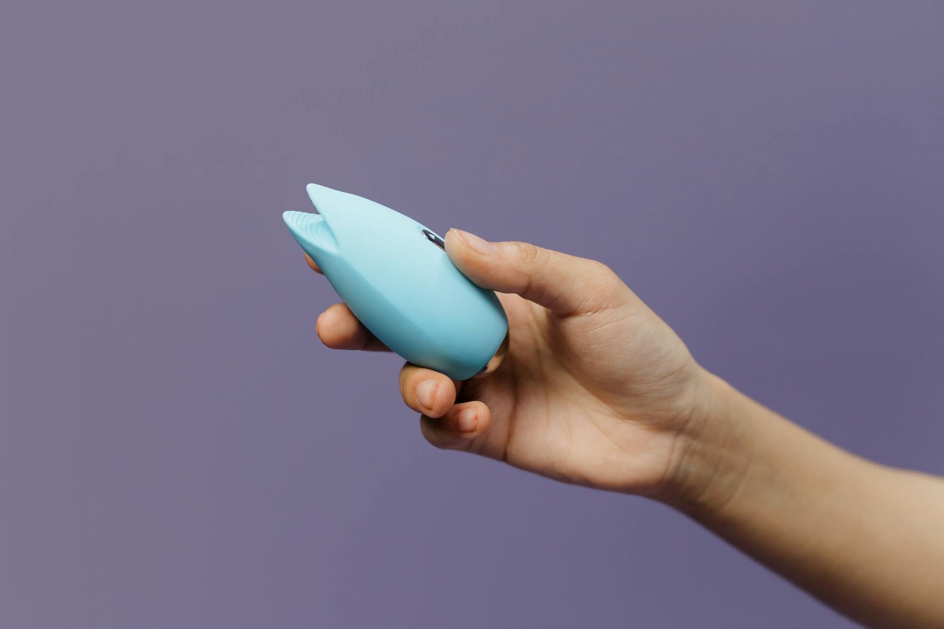 A blue silicone lemon vibrator held in hand against a purple background, designed for gentle clitoral stimulation