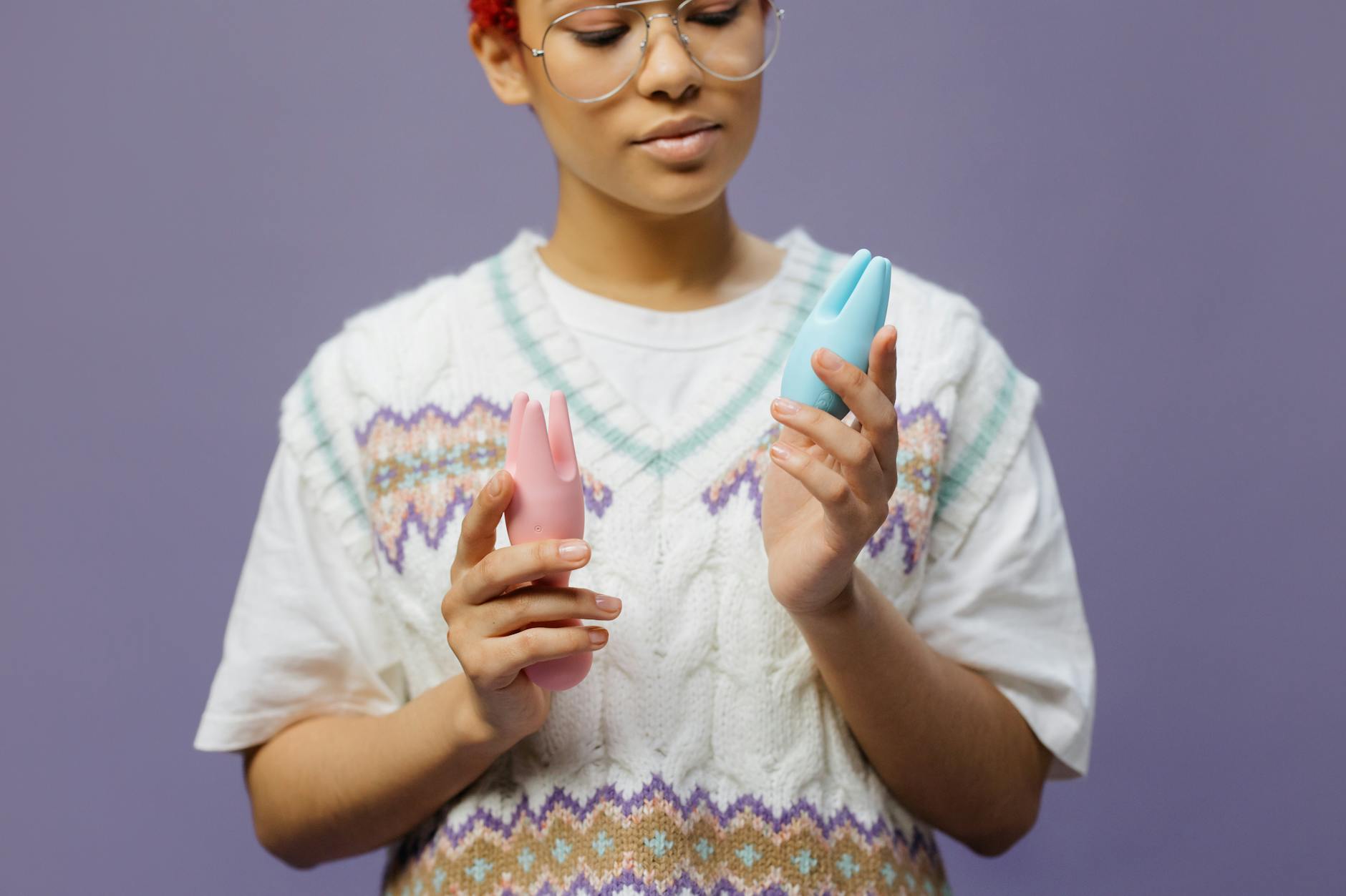 Woman holding blue and pink silicone vibrators in thoughtful contemplation